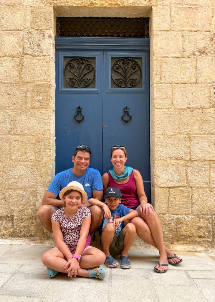Our family of 4 sitting in front of a large blue door. 