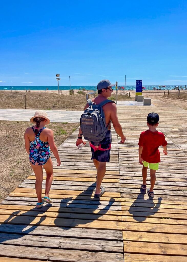 Dad and two young kids walking along the boardwalk at a beach in Castelldefels, Spain