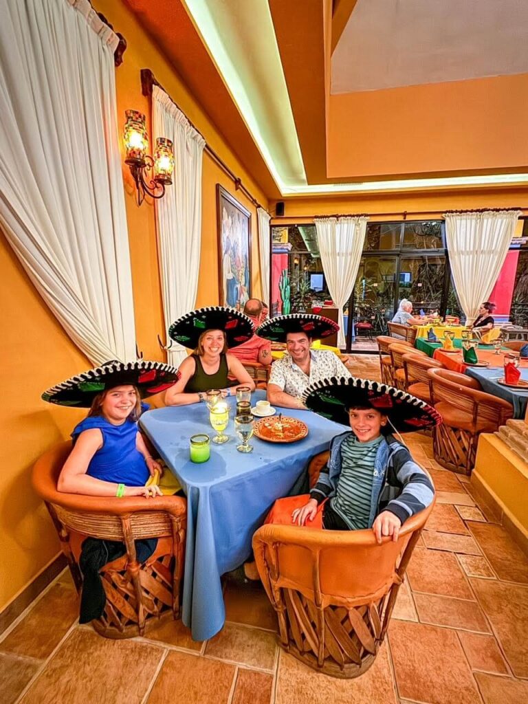 family with mom, dad and 2 young kids sitting in a colorful Mexican themed restaurant wearing sombreros. 