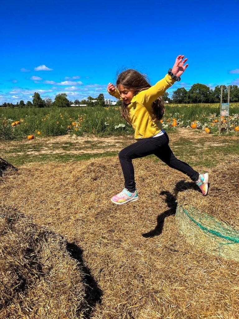 A young girl leaping from one hay bale to another 