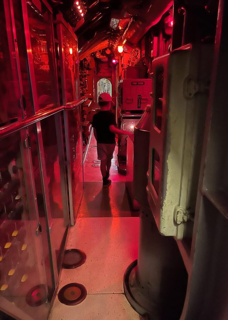 Looking down a narrow hallway of a submarine, lit up with red lights