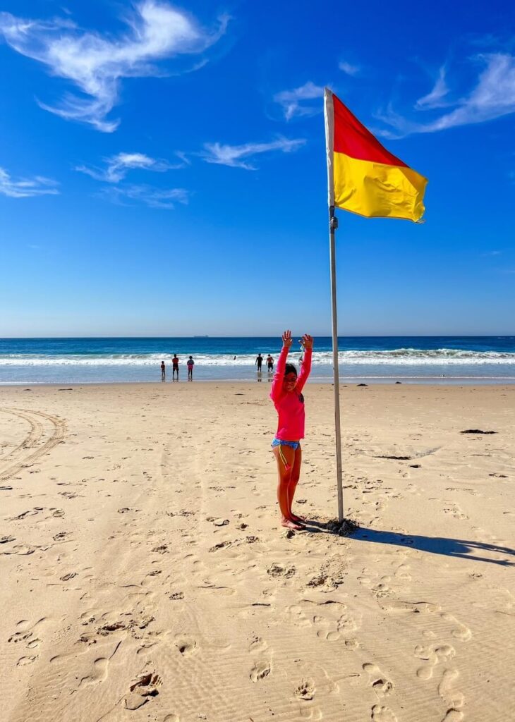 Beach in Australia with the red and yellow flag. A young girl pointing to the flag