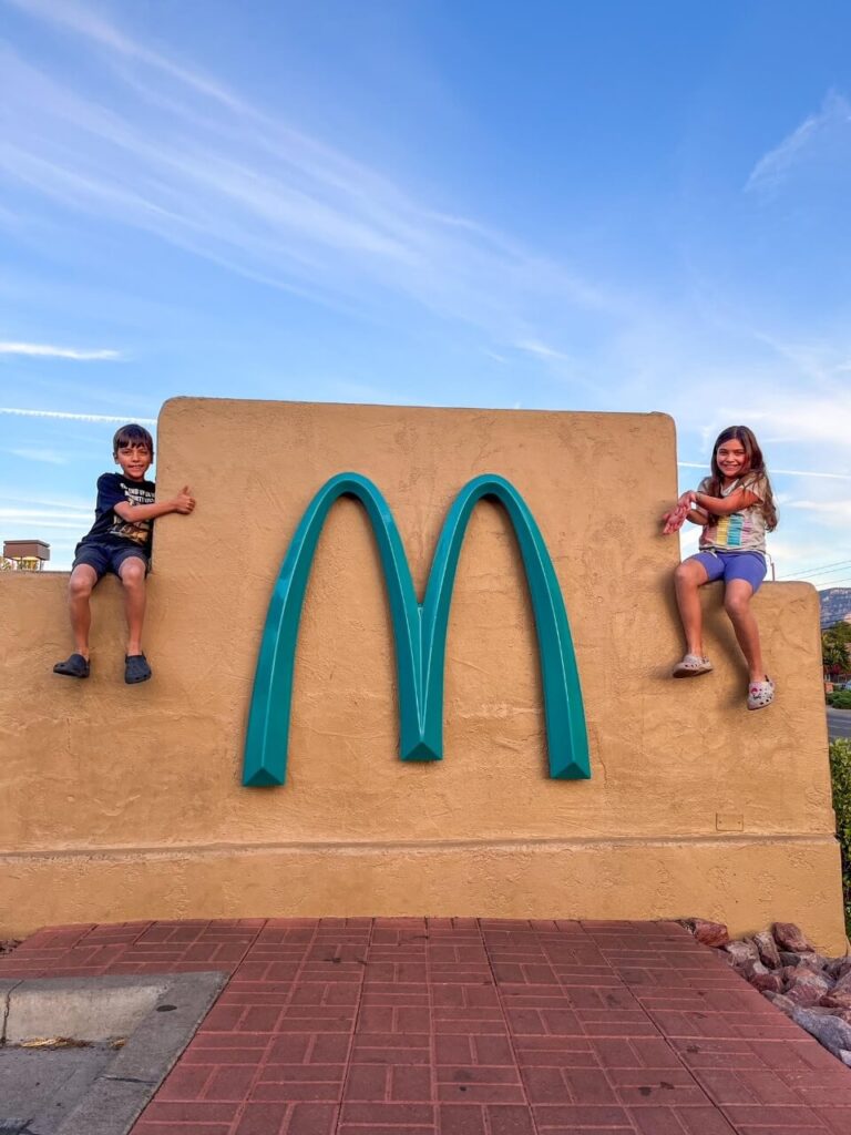 2 kids sitting on a wall beside the McDonald's arches in blue.