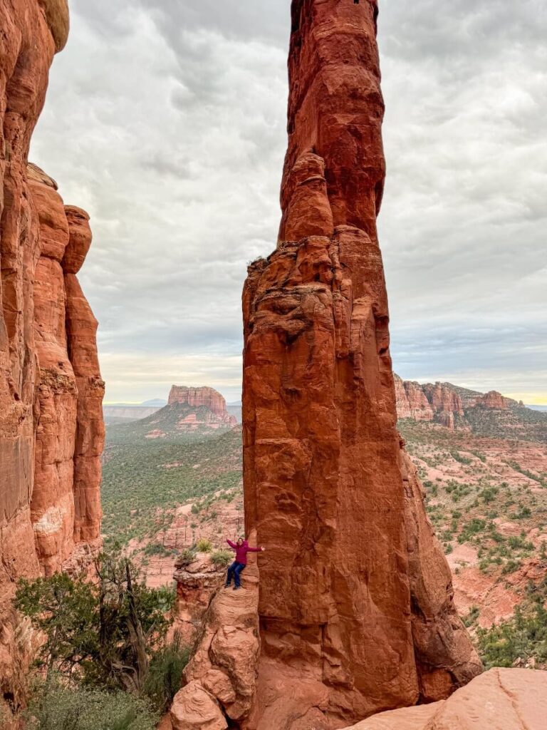 Large Red Rocks in Sedona, woman sitting on lower rock in the distance with pink jacket on.