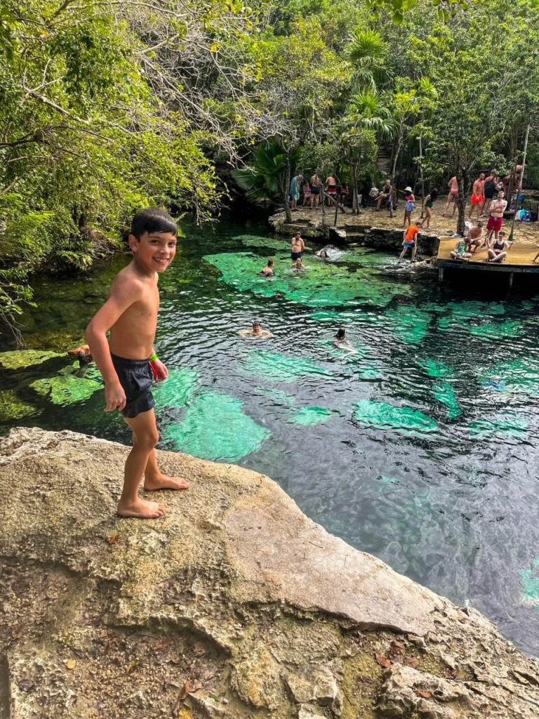 Boy standing at the top of the cliff at cenote azul getting ready to jump into the water below. 