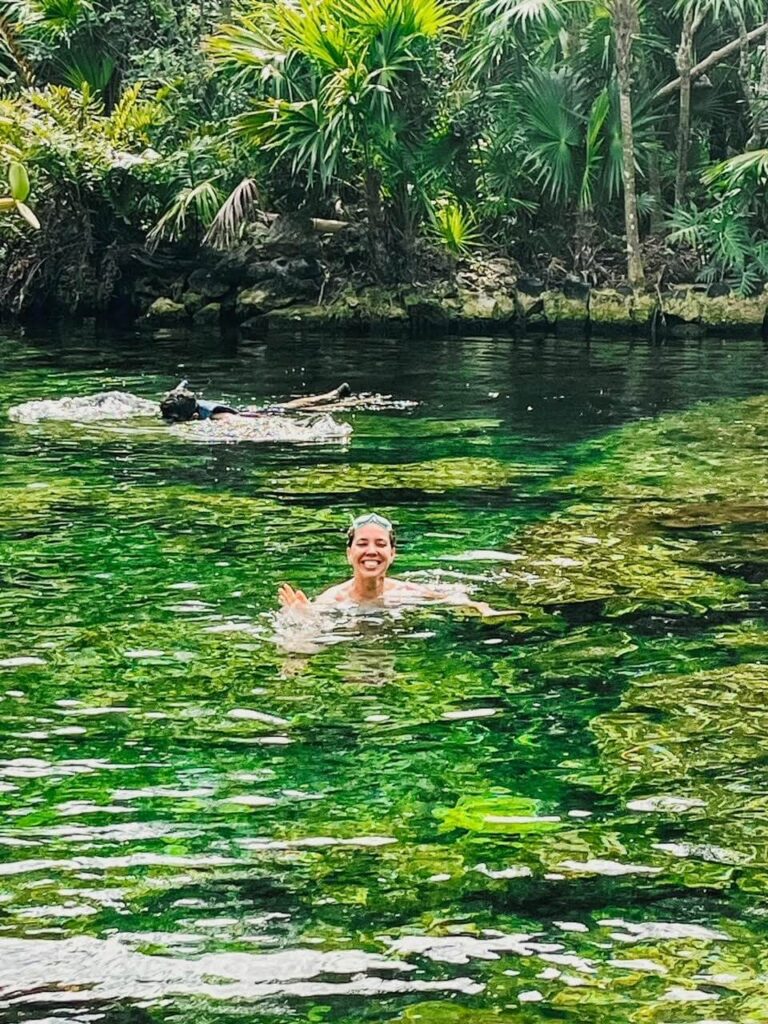 woman swimming in the cenote water, waving. 