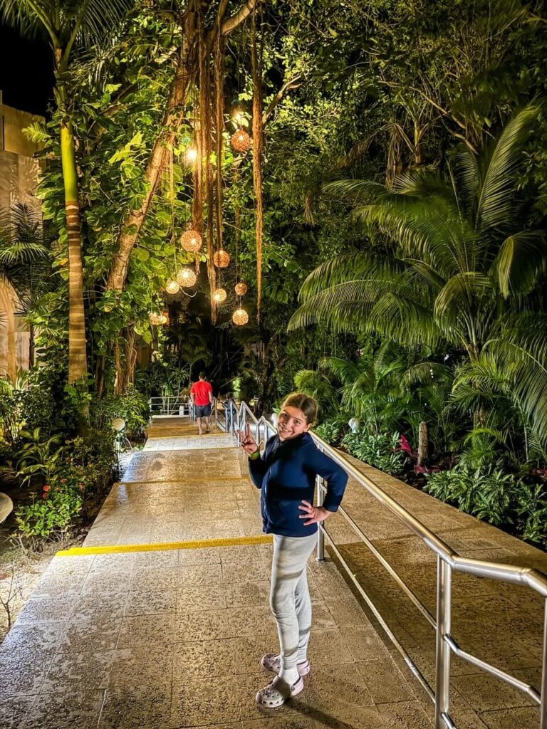 Night photo of Viva Maya, girl posing along a path lit up with lanterns, surrounded by palm trees. 