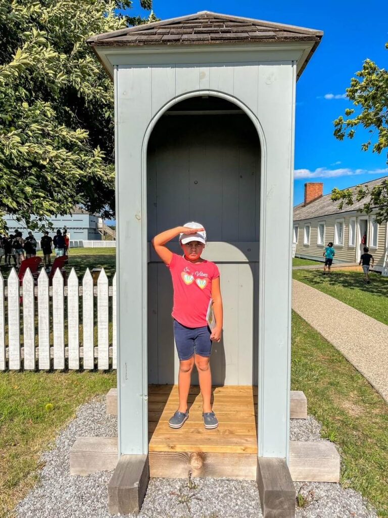 A little girl standing in a soldier booth pretending to be a soldier at Fort George in Niagara on the Lake