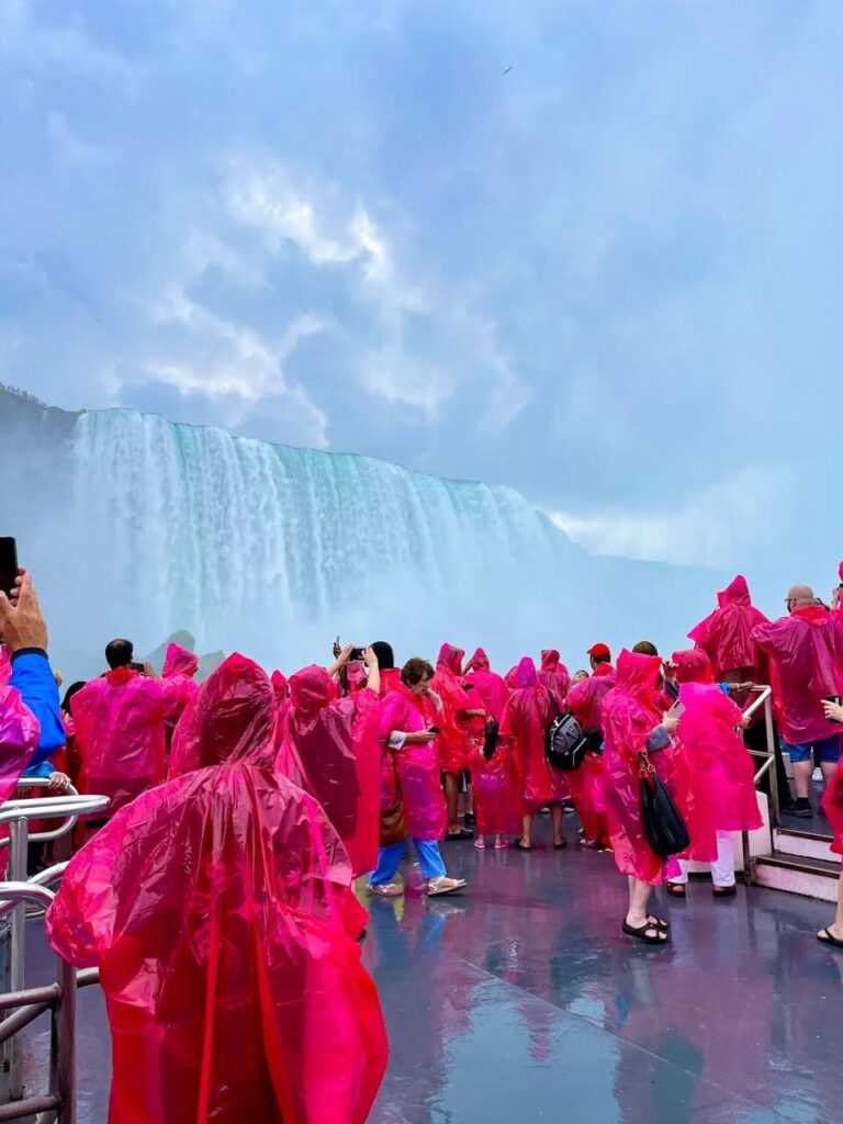 Standing on the Hornblower also known as Niagara City Cruises. Other people in the boat are dressed in red ponches. Niagara Falls right beside the boat.