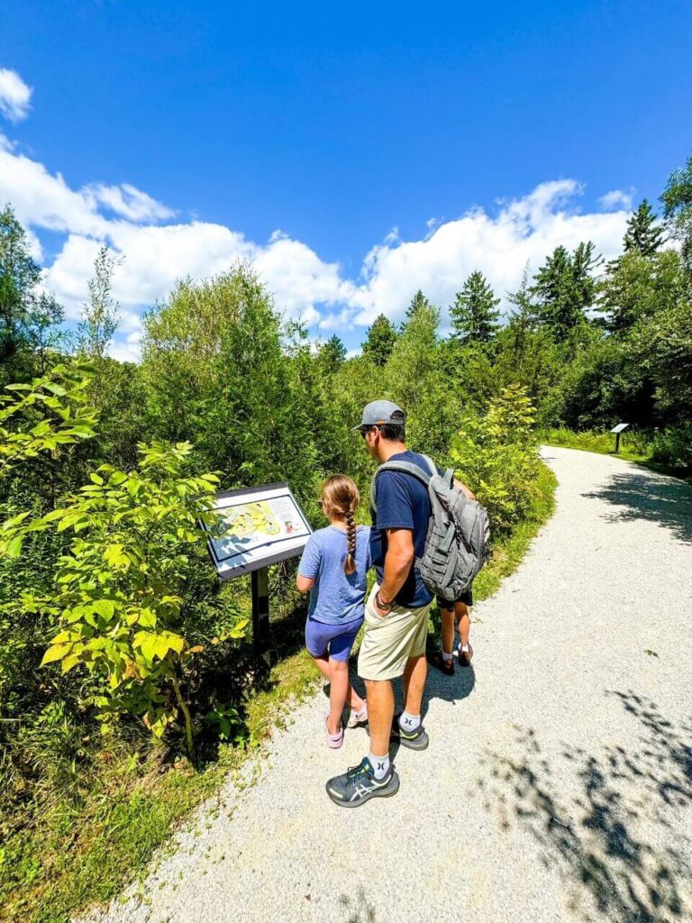 A family reading a sign on the storybook trail at Terra Cotta Conservation. Surrounded by trees.