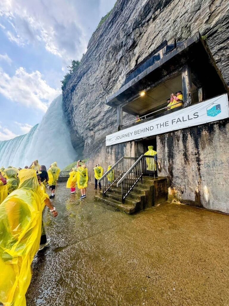 Standing at the bottom side of Niagara Falls, people wearing yellow ponchos. the ground is wet. 