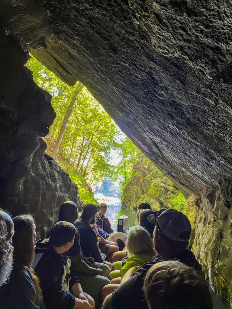 A group of people on a long skinny boat with caves all around at Penn's Cave