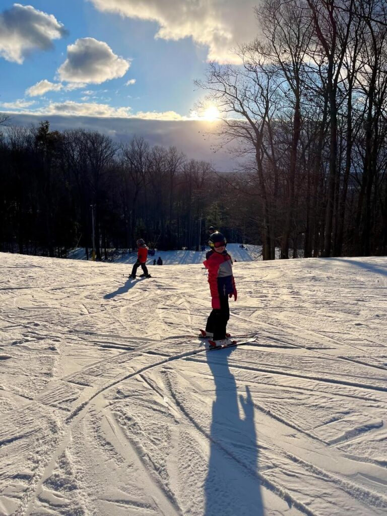 2 kids learning to ski, standing on skis at the top of a mountain at horseshoe resort.