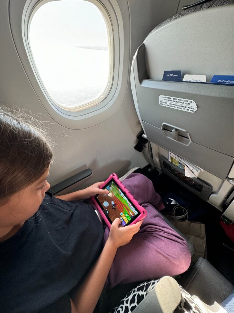 Girl sitting on a plane playing a game on her tablet. 