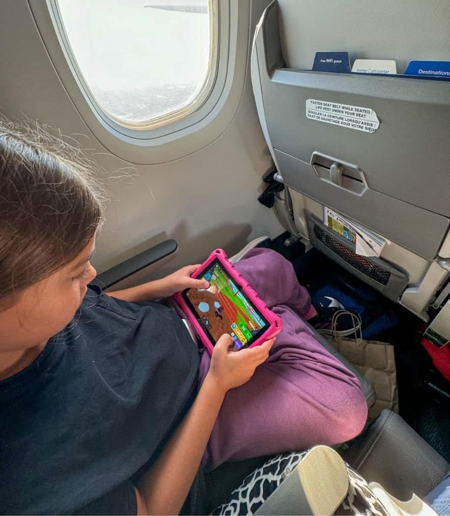 Girl sitting on a plane, playing a game on an Amazon Fire Tablet