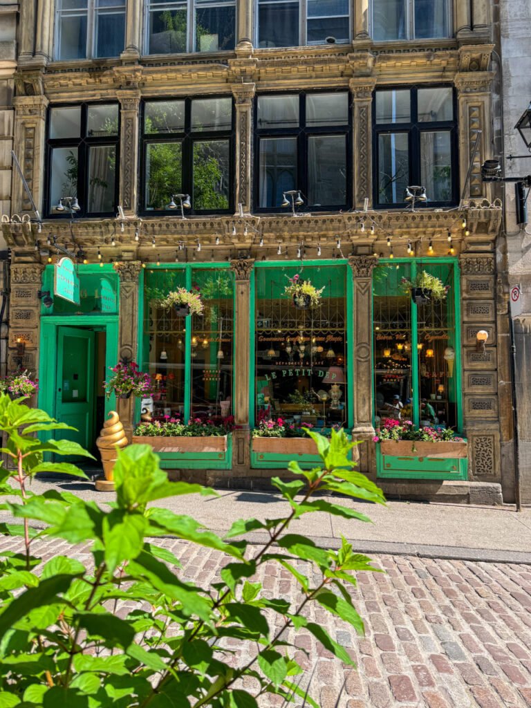 a French cafe on the cobblestone streets of Montreal with green framed windows and flower baskets outside.