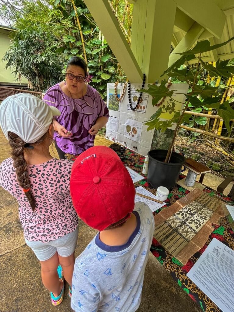 2 kids listening to a woman talk about traditional hawaiian toys